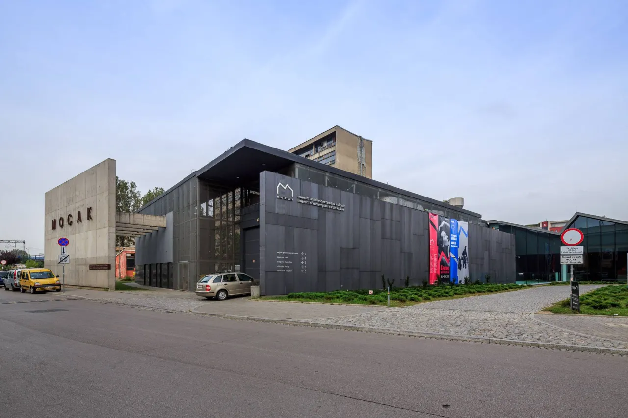 Nowoczesny budynek muzeum sztuki wsp&oacute;łczesnej w Krakowie MOCAK z betonowym napisem i szarymi panelami.