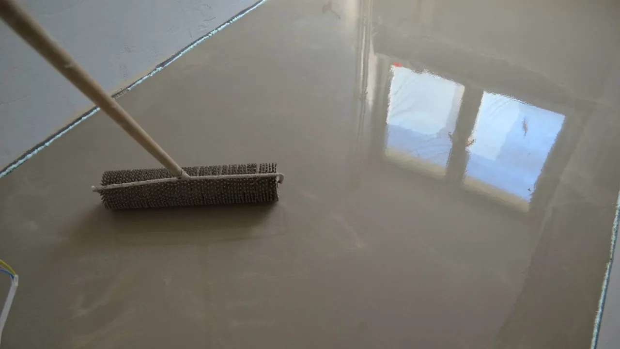 Wylewka samopoziomująca w trakcie aplikacji. Wałek do odpowietrzania wygładza świeżą masę, kt&oacute;ra lśni odbijając światło okien.