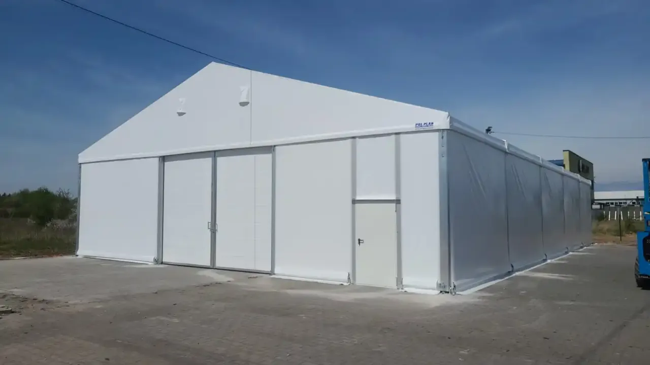 Duży biały namiot magazynowy z drzwiami i bramą przesuwną. Czy postawienie namiotu magazynowego wymaga pozwolenia na budowę?