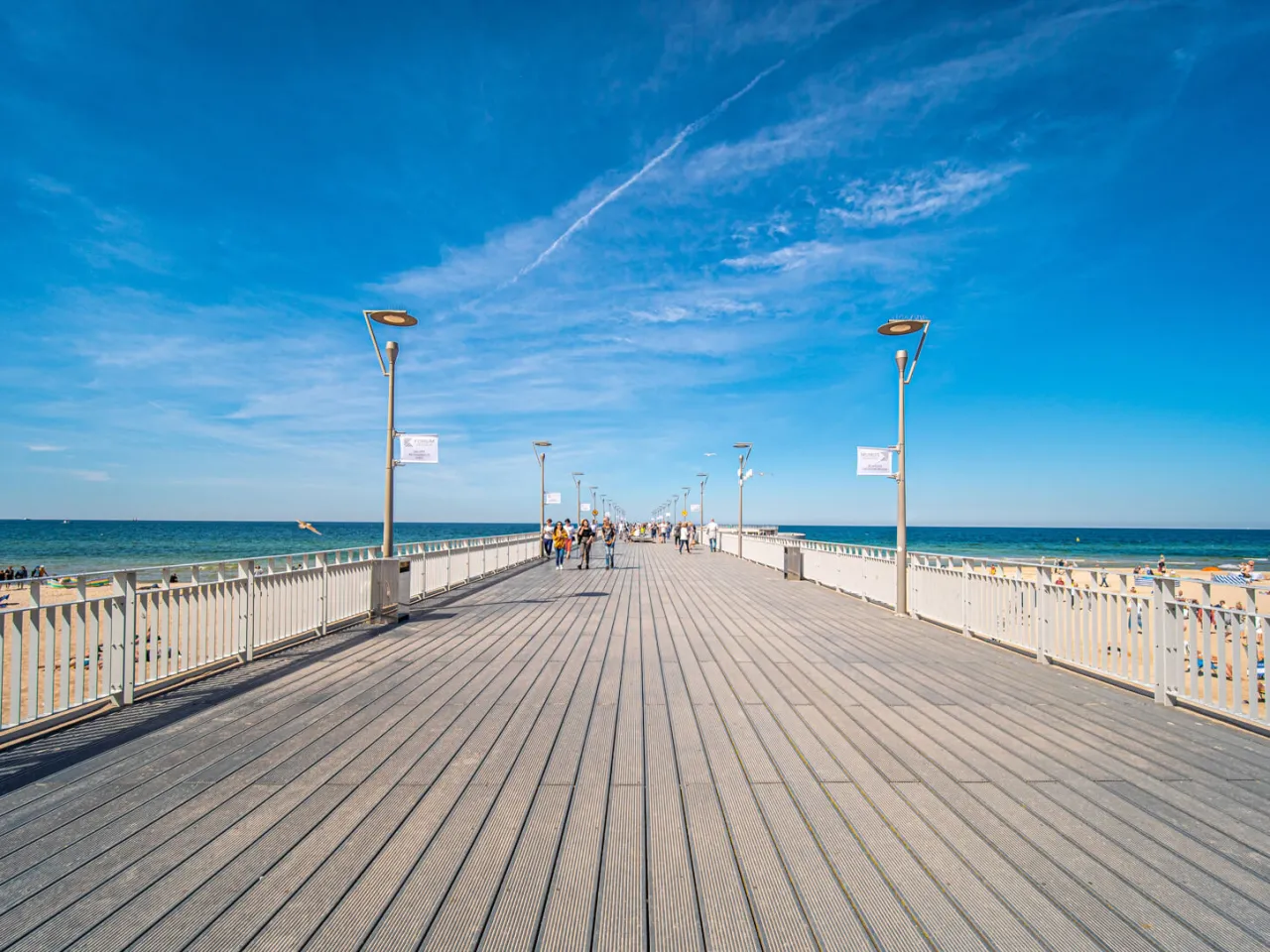 Spacer w Kołobrzegu, z ludźmi spacerującymi po drewnianej nawierzchni. Czy molo w Kołobrzegu jest płatne? Dziś można przejść bez opłat.