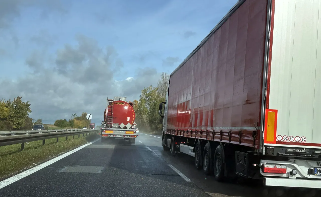 Ciężar&oacute;wka z czerwoną cysterną jedzie po mokrej drodze. Zbliża się do znaku ograniczenia prędkości 90 km/h. Uważaj na mandat za wyprzedzanie tirem.