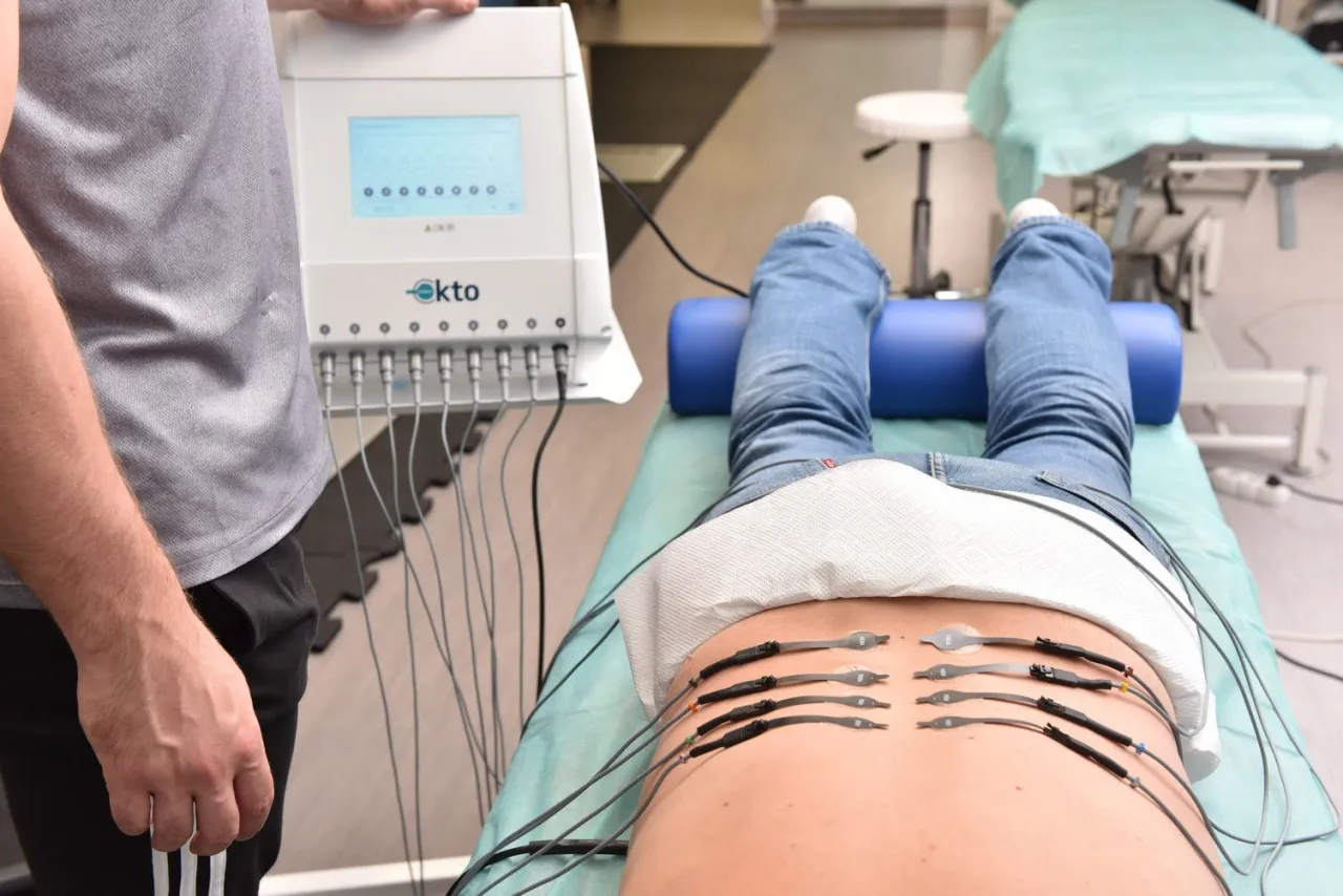 Fizjoterapeuta używa elektroterapii do leczenia bólu pleców. Pacjent leży na kozetce, a elektrody podłączone są do jego kręgosłupa.