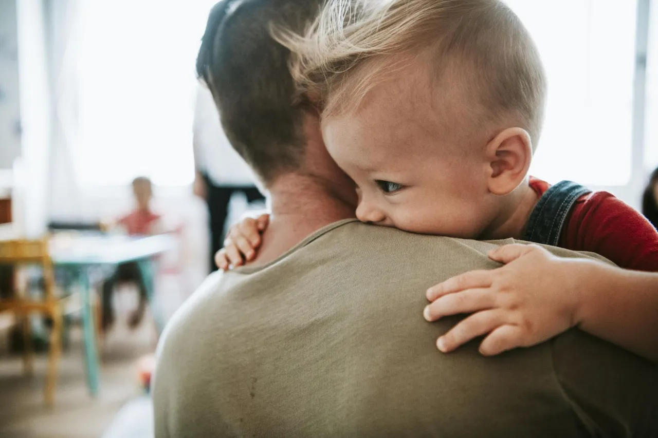 Dziecko wtulone w tatę. Zastanawiasz się, do kogo przysługuje dofinansowanie do żłobka?