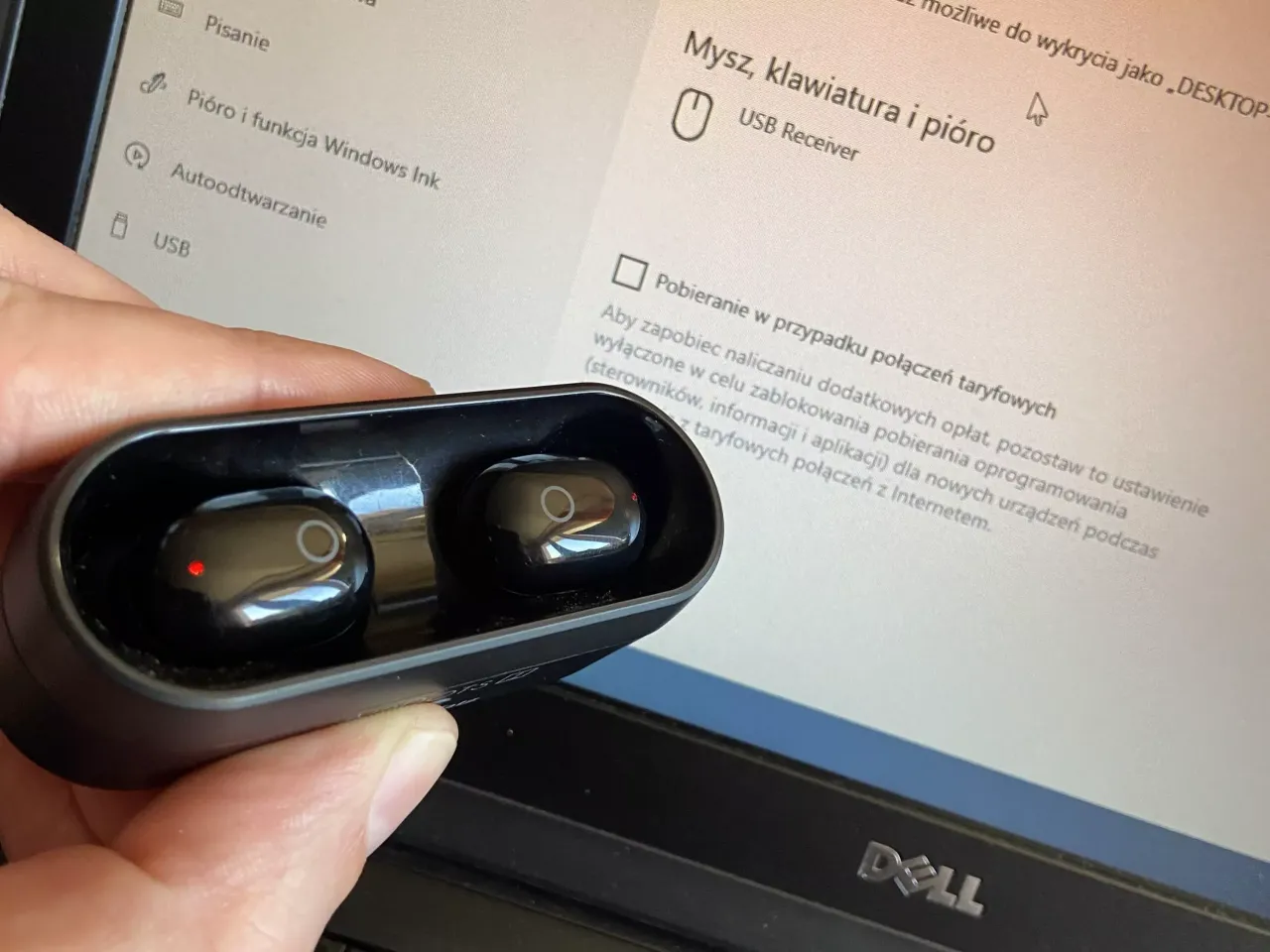 Czarna ładowarka ze słuchawkami w dłoni, na ekranie laptopa widoczne ustawienia Bluetooth. Dowiedz się, jak sparować słuchawki z laptopem.