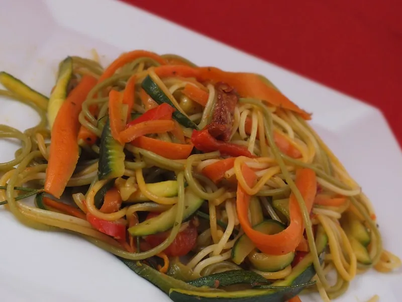kolorowe spaghetti z warzywami na białym talerzu