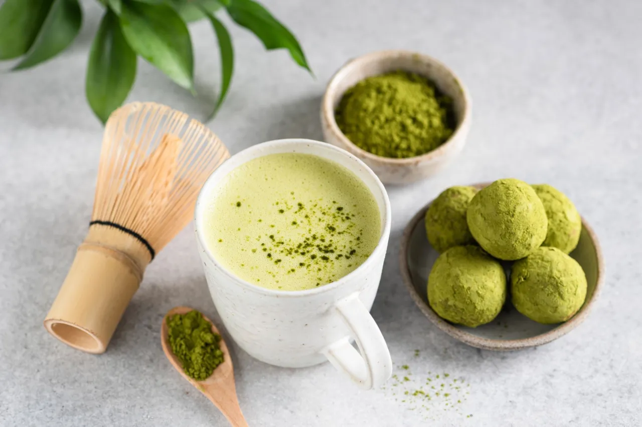 Aromatczna matcha w kubku, obok bambusowa miotełka i kulki. Idealna na pobudzenie i relaks. Wiesz, na co dobra jest matcha!