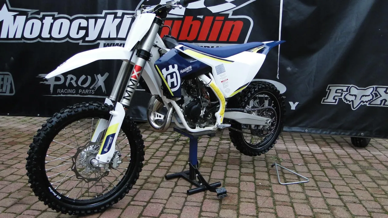 Husqvarna TC 125 gotowy do akcji. Biało-niebieski motocykl crossowy z żółtymi akcentami.