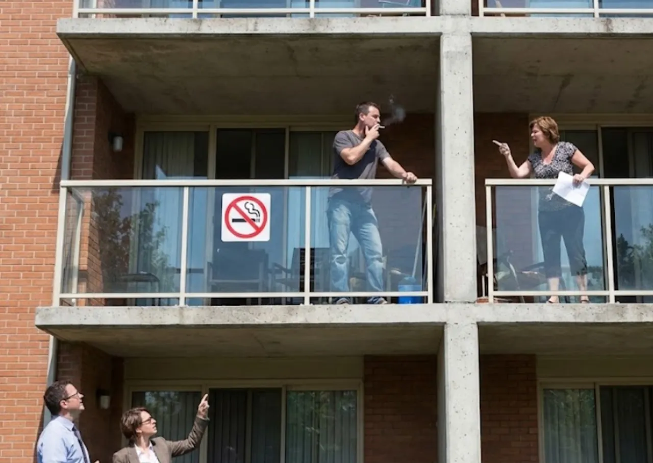 Mężczyzna pali na balkonie, mimo znaku zakazu palenia papierosów. Sąsiadka z wyciągniętym palcem zwraca mu uwagę.