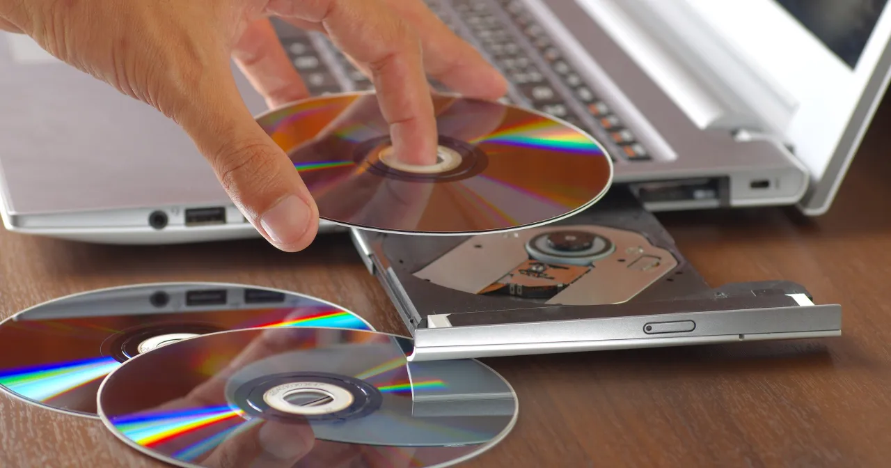 Dłoń wkłada płytę do napędu laptopa, przygotowując się do nagrania danych. Program do wypalania płyt ułatwia ten proces.