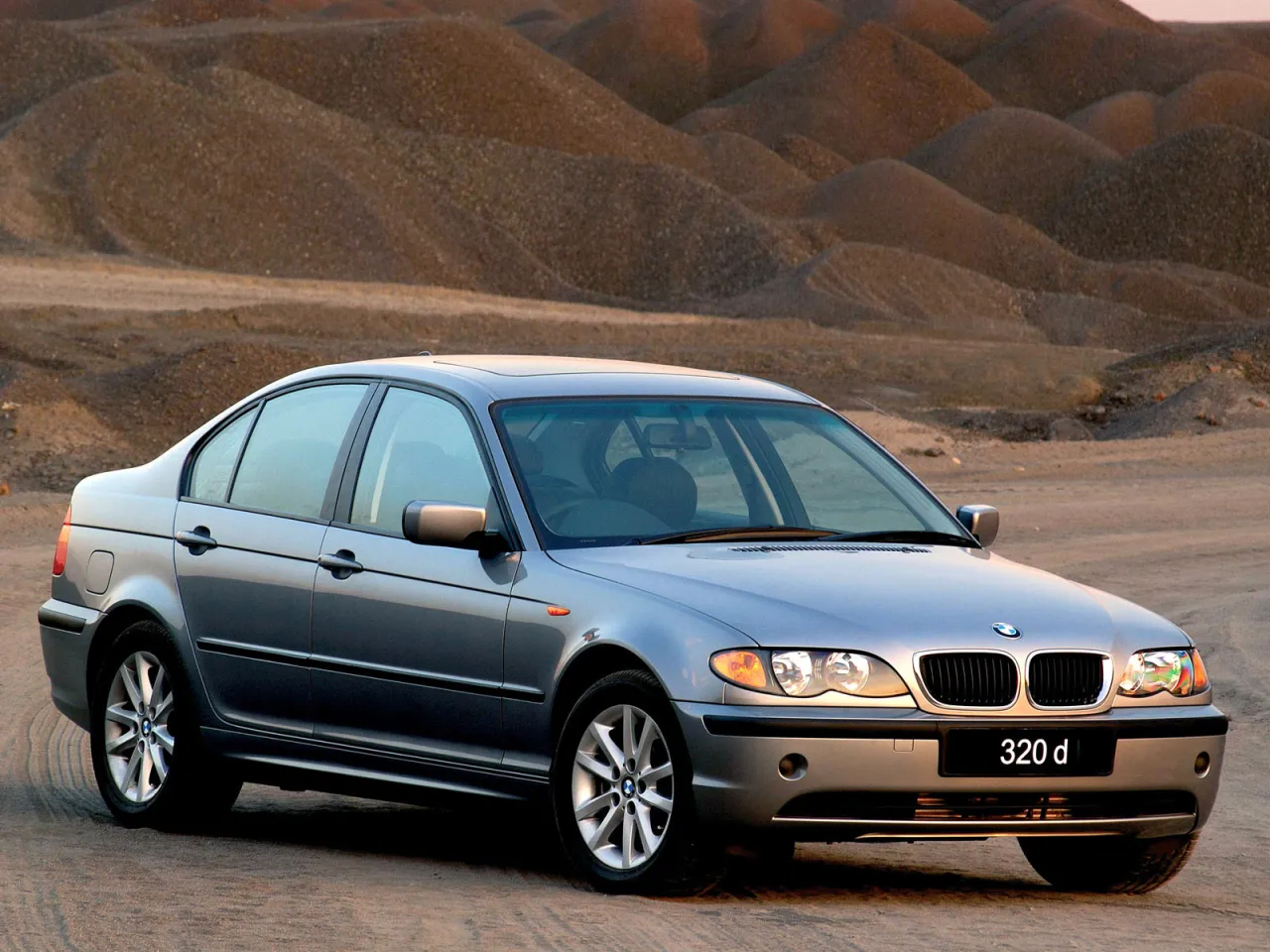Srebrne BMW E46 320d, popularne w latach produkcji 1998-2007, na tle pustynnego krajobrazu.