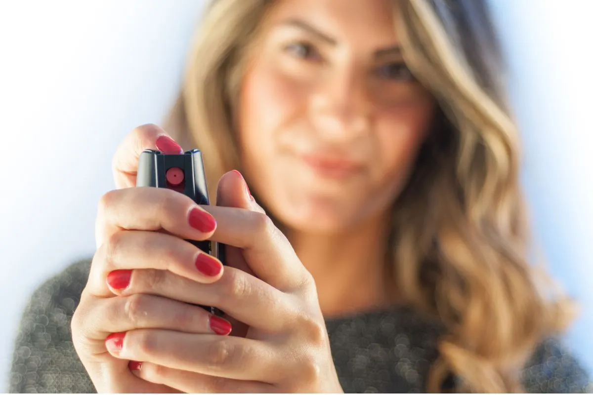 Kobieta z czerwonymi paznokciami trzyma gaz pieprzowy, gotowa do użycia w sytuacji zagrożenia.
