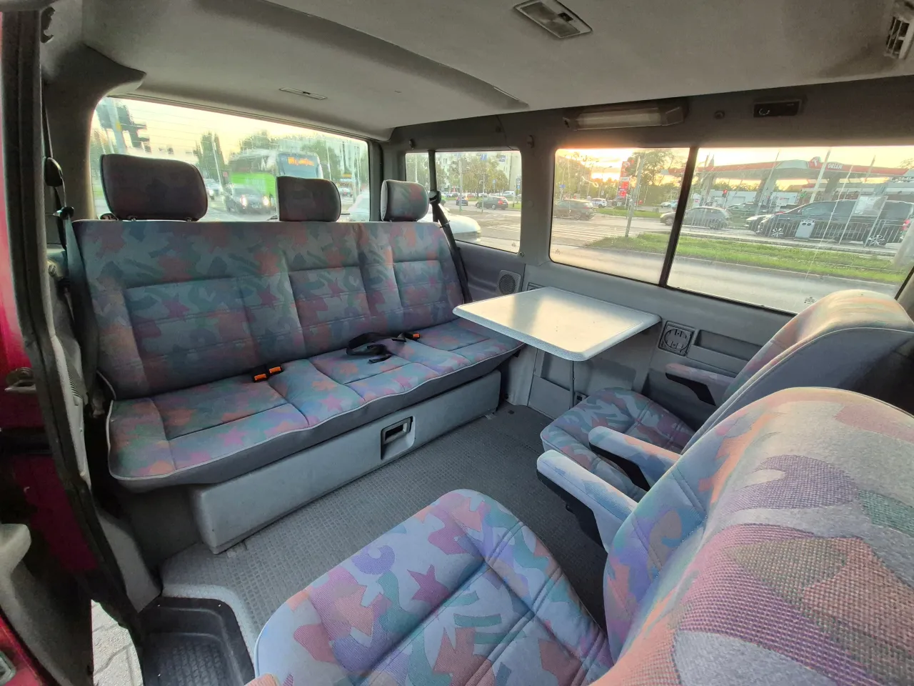 Wnętrze busa z kolorowymi siedzeniami i stolikiem. W tle widać stację Orlen i ulicę. Jaki bus w benzynie?