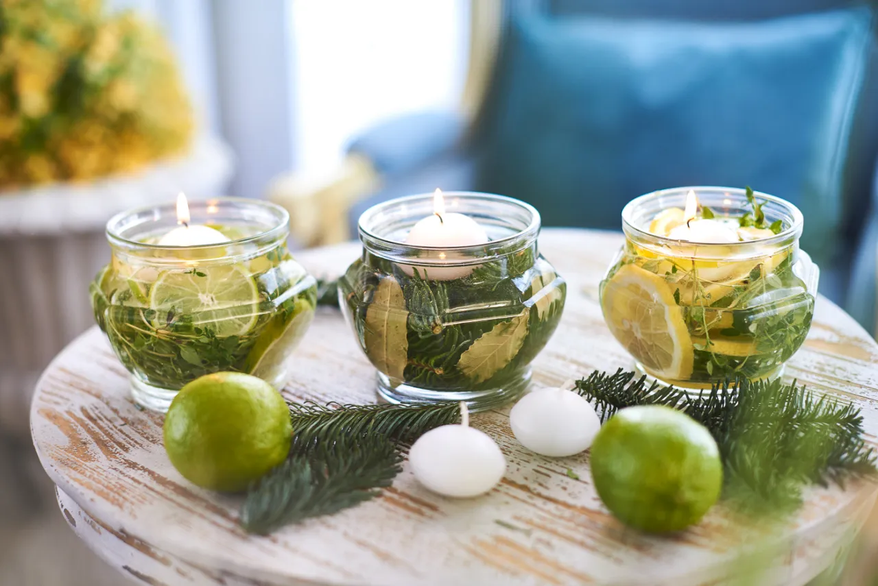 Jak zrobić domowy zapach do łazienki? Woda z cytryną, limonką i ziołami w słoikach z pływającymi świecami.
