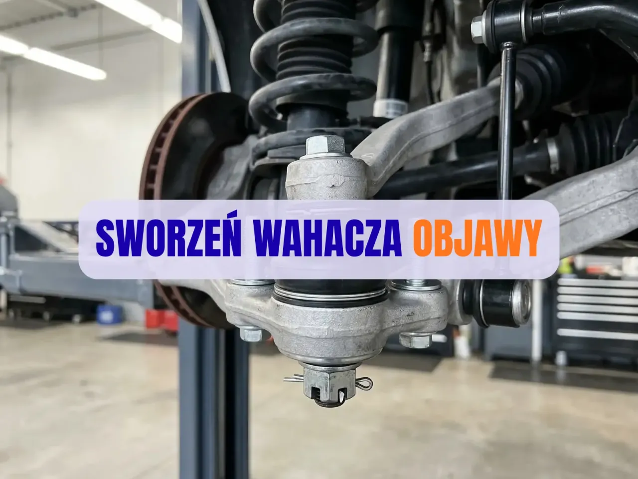 Widok na zawieszenie samochodu z widocznym sworzniem wahacza. Tekst na obrazku: 