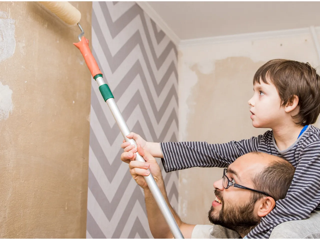 Ojciec i syn malują ścianę. Czy ściana pod tapetę musi być gładka? Chłopiec pomaga tacie, trzymając wałek.