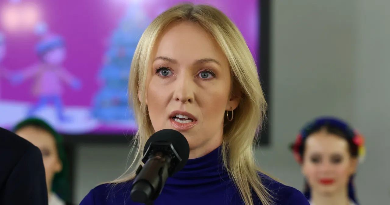 Urszula Brzezińska Hołownia, mówiąca do mikrofonu, w tle dzieci w strojach ludowych.