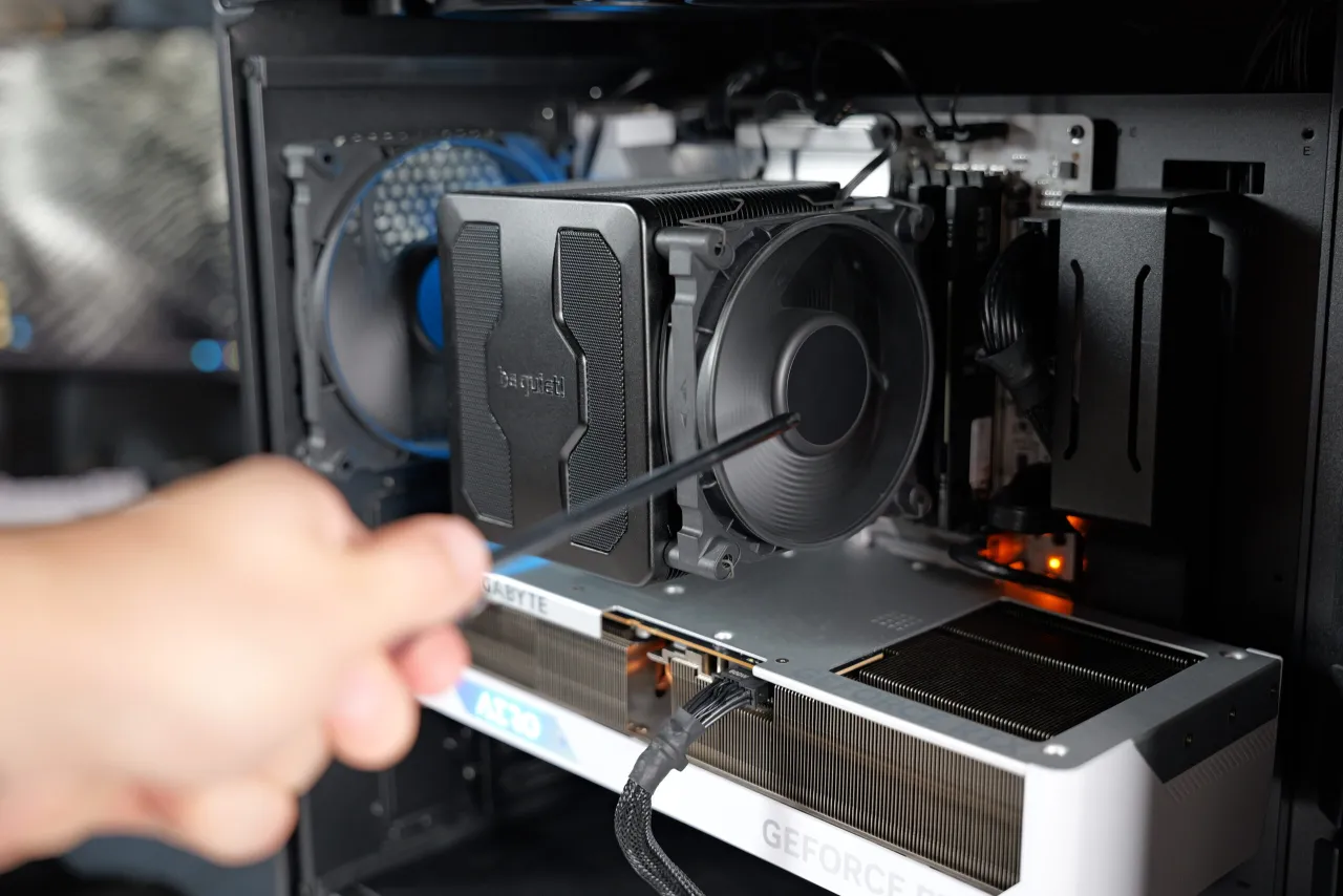Wnętrze komputera z widocznymi częściami: cooler CPU, karta graficzna Gigabyte AERO, wentylatory i okablowanie. Dłoń z narzędziem przy coolerze.