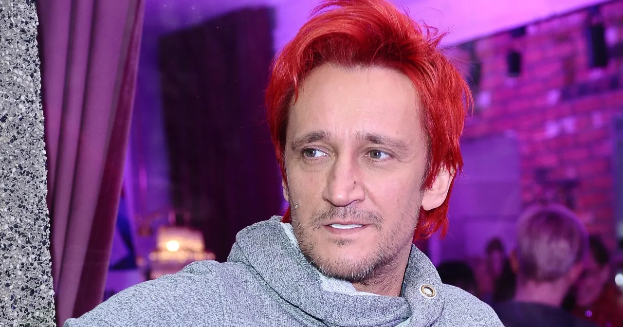 Michał Wiśniewski z charakterystycznymi rudymi włosami i w szarym swetrze. Choć trudno ocenić ile wzrostu ma Michał Wiśniewski na tym zdjęciu, jego charyzma jest widoczna.