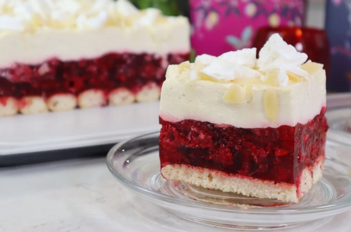Malinowa rozkosz bez pieczenia: warstwy biszkoptu, galaretki z malinami i kremu, ozdobione bitą śmietaną i płatkami migdałów.