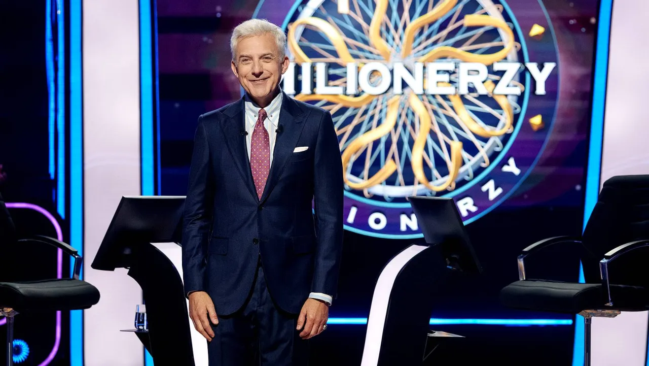 Uśmiechnięty prowadzący w garniturze na tle logo 