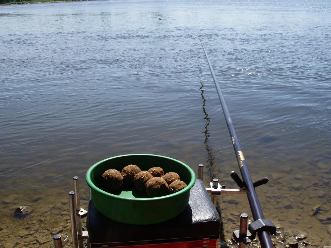 Zielona miska z kulkami zanęty, idealna na płoć, czeka obok wędki nad spokojną wodą.