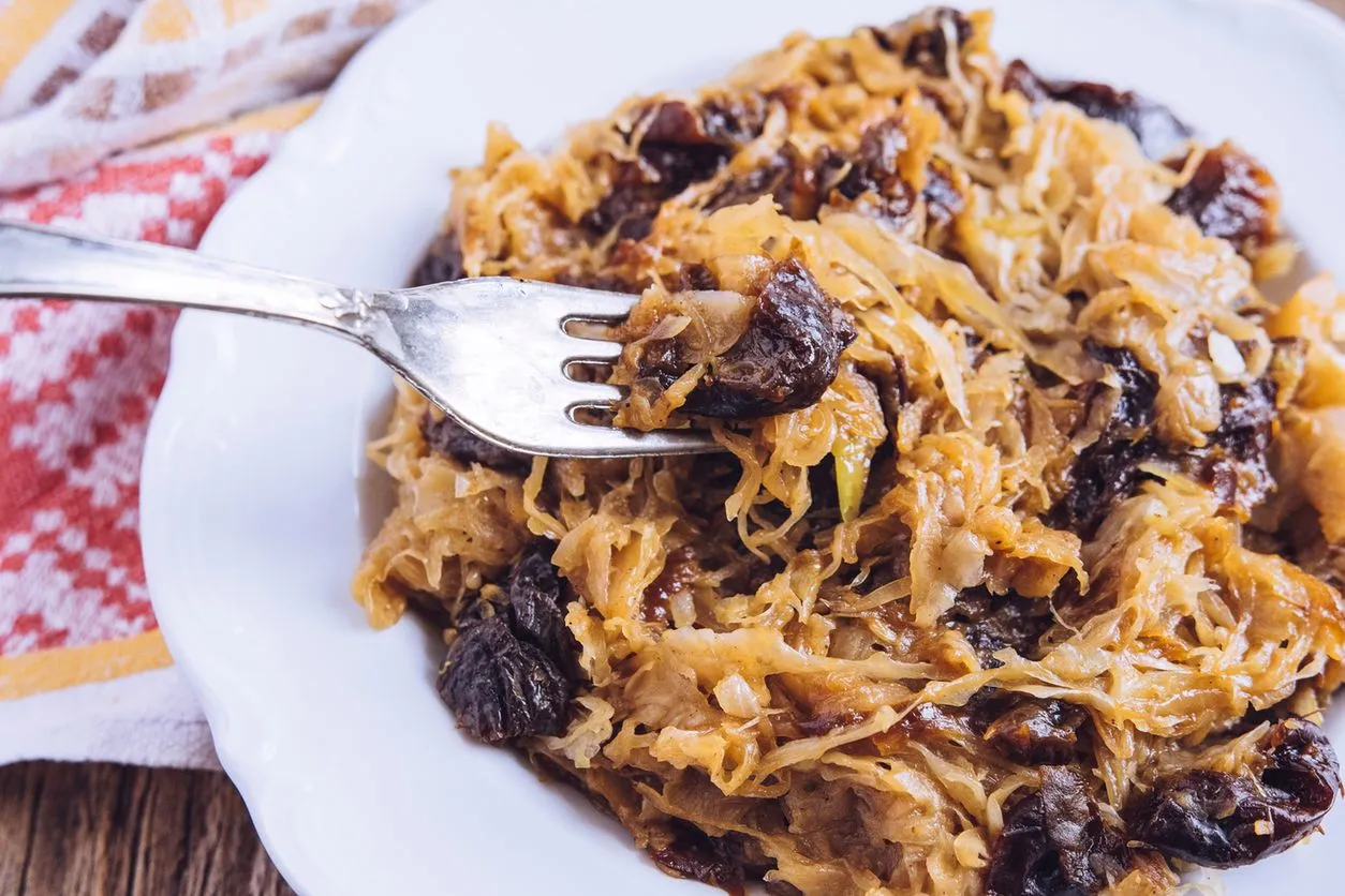 Talerz pełen bigosu z suszonymi śliwkami i grzybami. Idealne przyprawy do bigosu podkreślają jego głęboki smak. Widelec nabiera porcję dania.