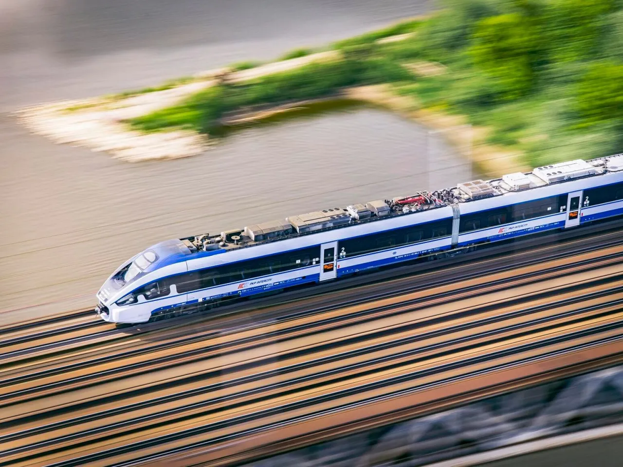 Szybki pociąg PKP Intercity mija rzekę. Zastanawiasz się, ile kosztuje bilet Intercity na podr&oacute;ż?
