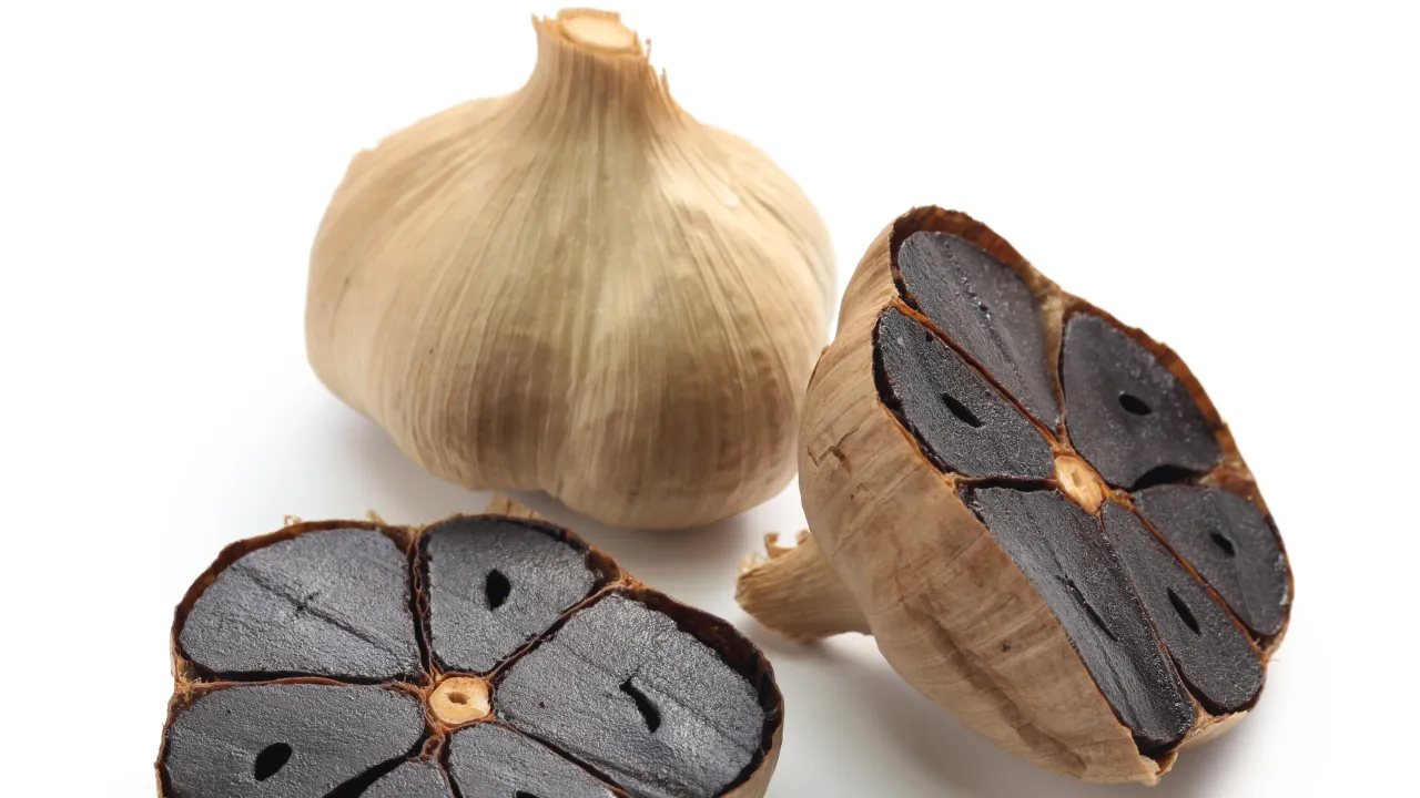 Cały i przekrojony czarny czosnek na białym tle. Dowiedz się, jak przechowywać czarny czosnek, by zachował świeżość i smak.