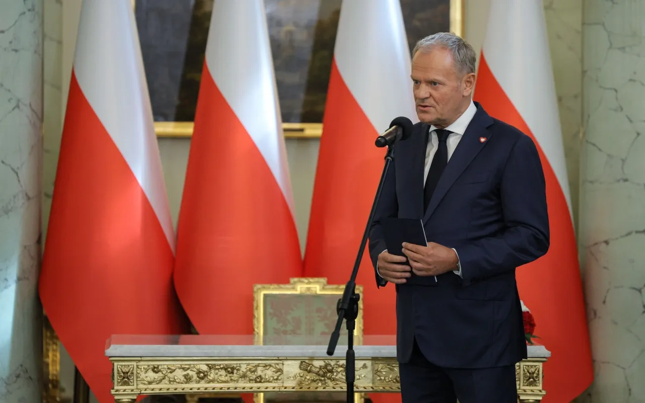 Donald Tusk przemawia na tle flag Polski. To on rządził w latach 2007-2015, kształtując losy kraju.