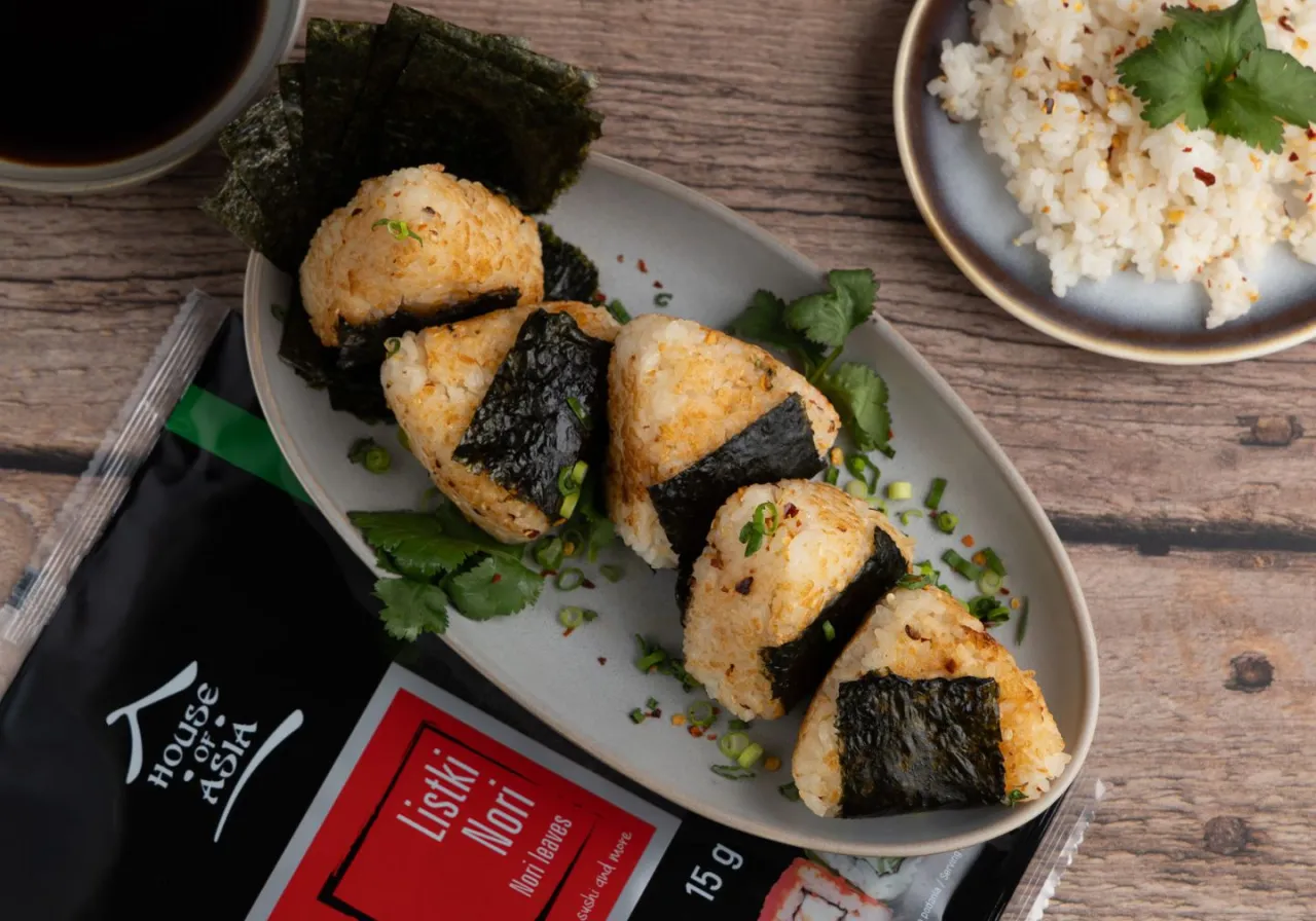 Pięć pysznych onigiri z ryżu, owiniętych w nori, gotowych do spożycia. Obok opakowanie listk&oacute;w nori.