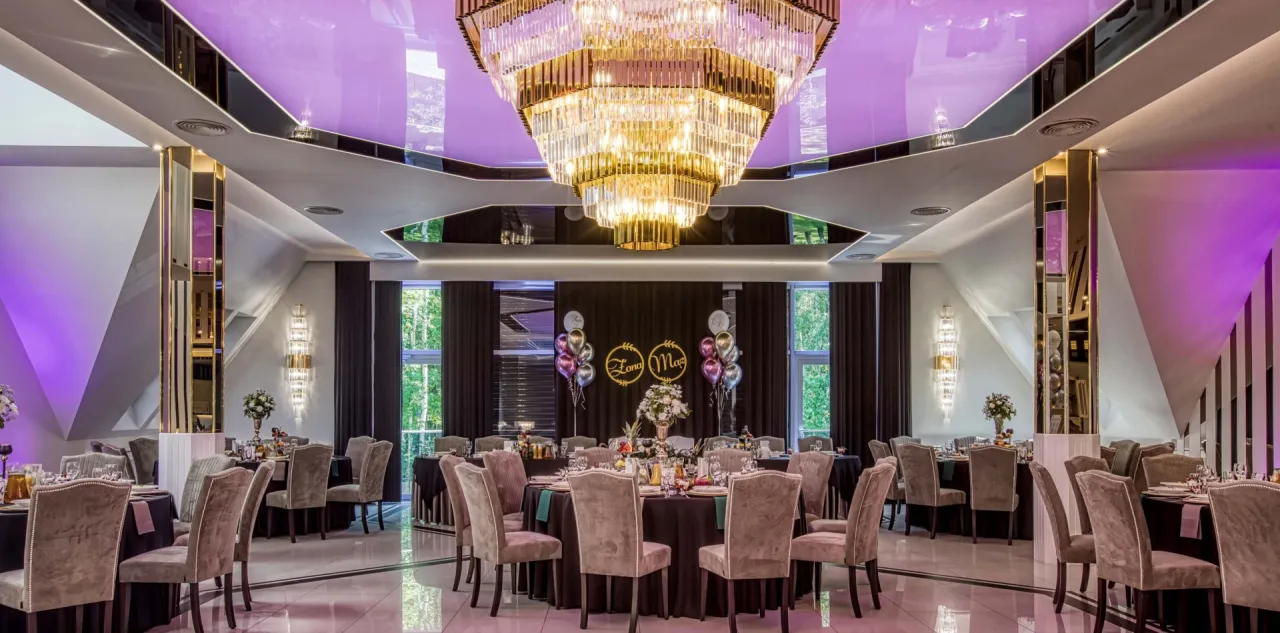 Elegancka sala weselna w białym domu, restauracji, hotelu & spa. Kryształowy żyrandol, fioletowe oświetlenie i dekoracje tworzą magiczną atmosferę.
