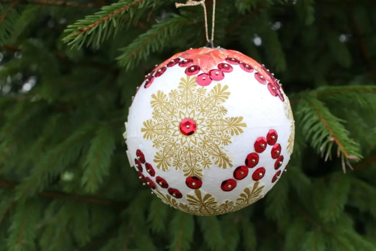 Ozdobiona złotymi wzorami i czerwonymi cekinami bombka DIY wisi na choince.