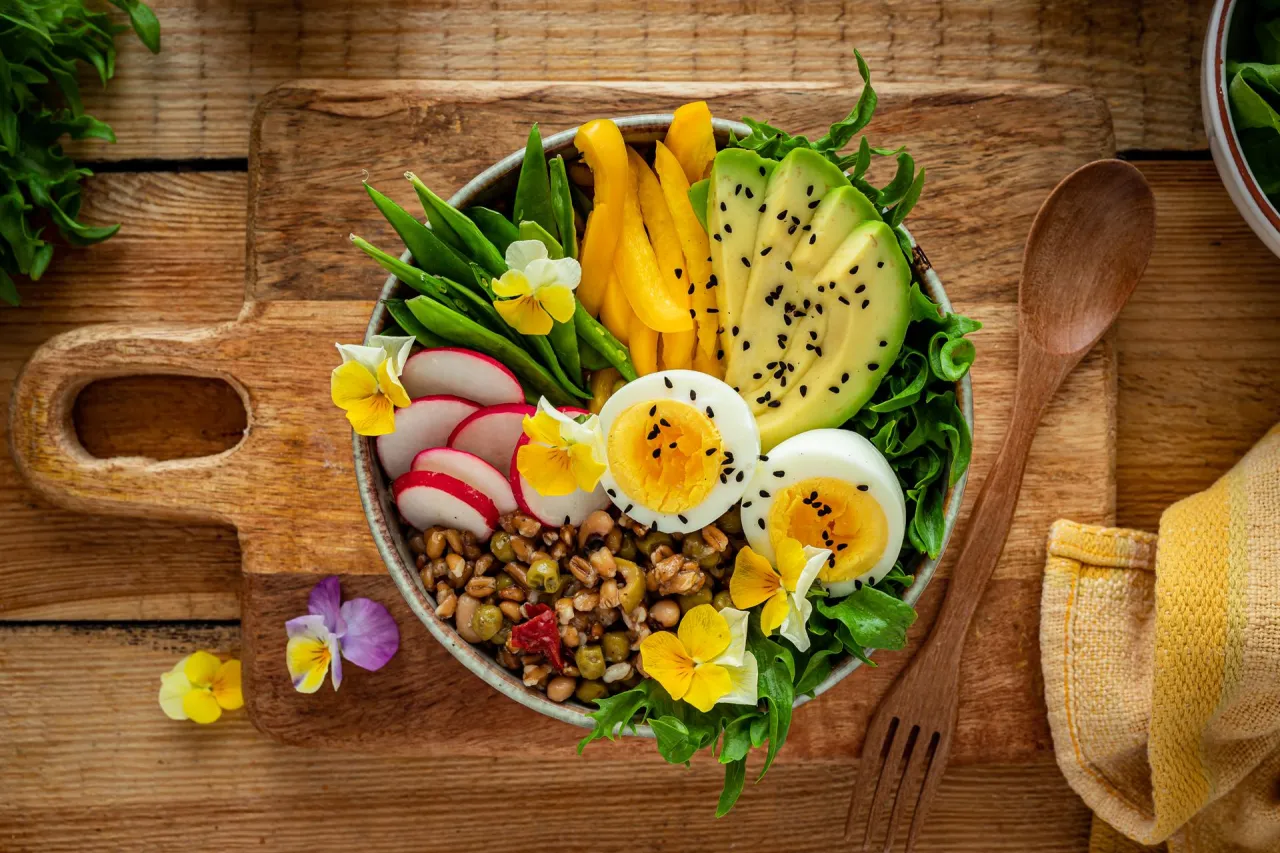 Kolorowy bowl co to? Pełen zdrowych składnik&oacute;w: soczewica, jajka, awokado, rzodkiewka, fasolka szparagowa i papryka. Udekorowany jadalnymi kwiatami.