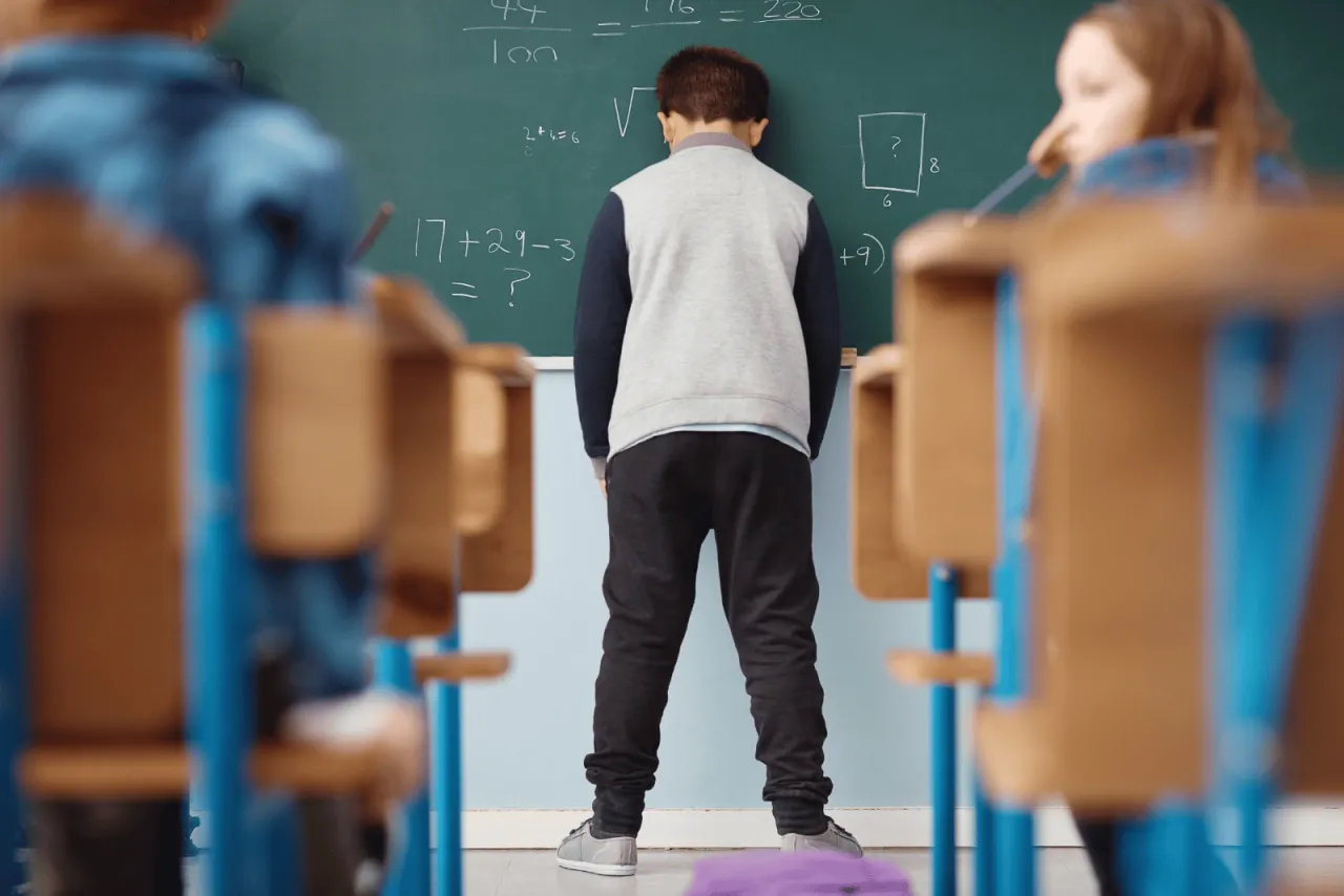 Chłopiec stoi przy tablicy, zamyślony nad zadaniem. Wskazówki, jak postępować z dzieckiem z fobią szkolną, mogą pomóc mu odnaleźć się w tej sytuacji.