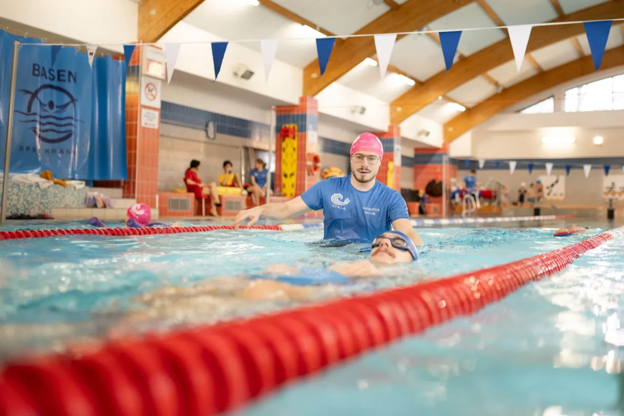 Instruktor pokazuje, jak nauczyć pływać dorosłego. Uczeń leży na plecach, a instruktor go asekuruje.