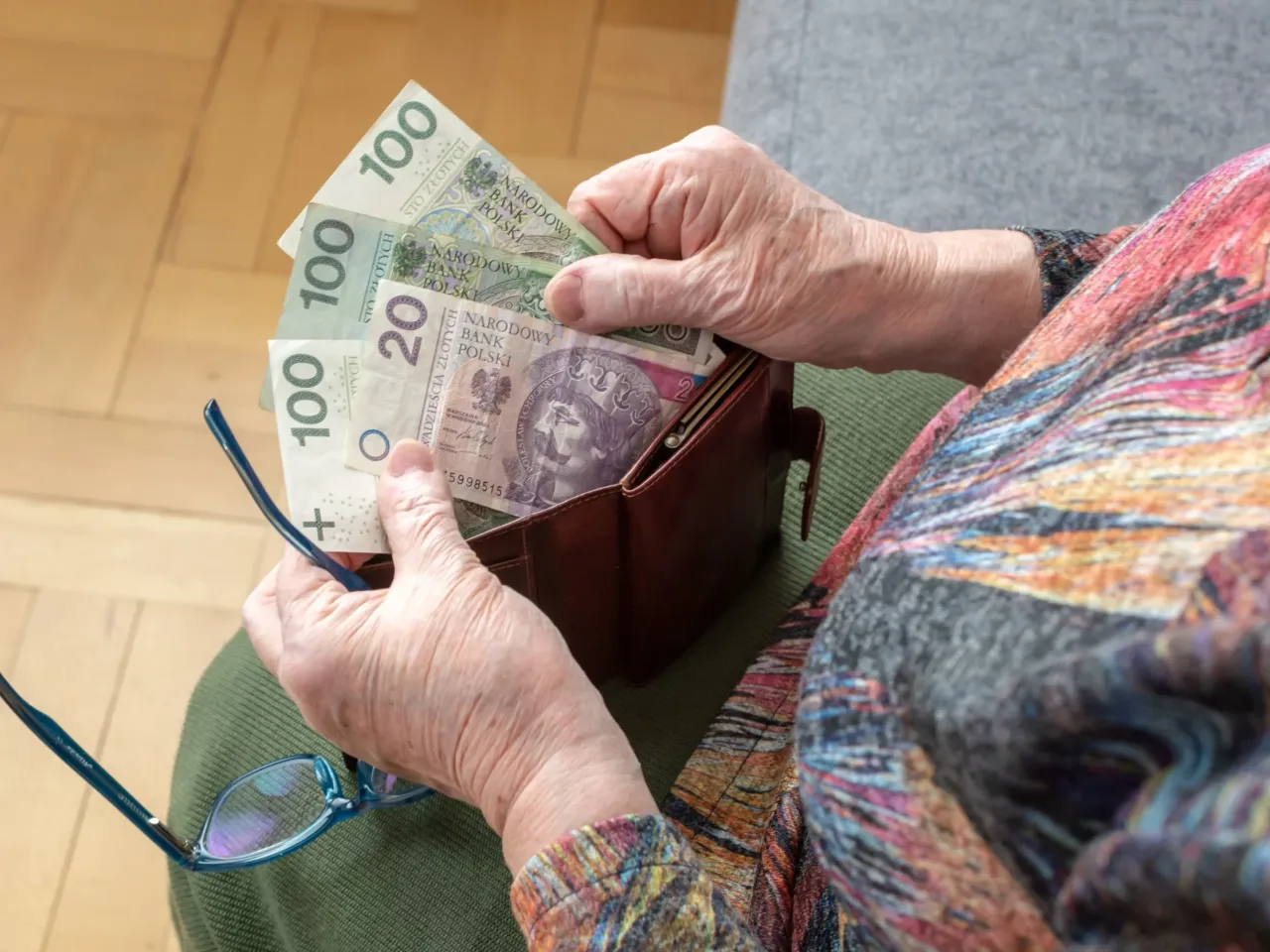 Dłonie starszej osoby chowają banknoty do portfela, kiedy listonosz przynosi emeryturę.