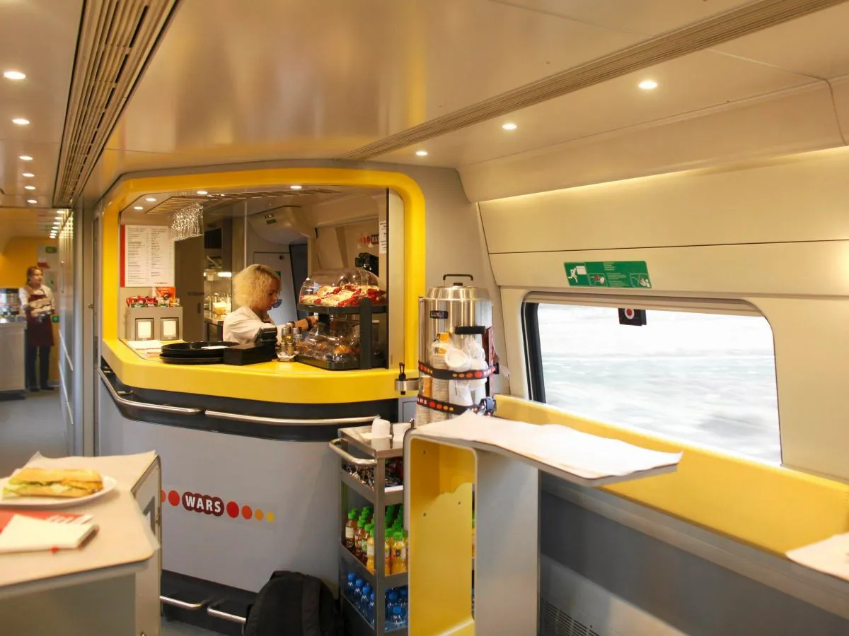 W pociągu jest WARS, gdy widzisz bar z jedzeniem i napojami. Kobieta za ladą serwuje klientom.