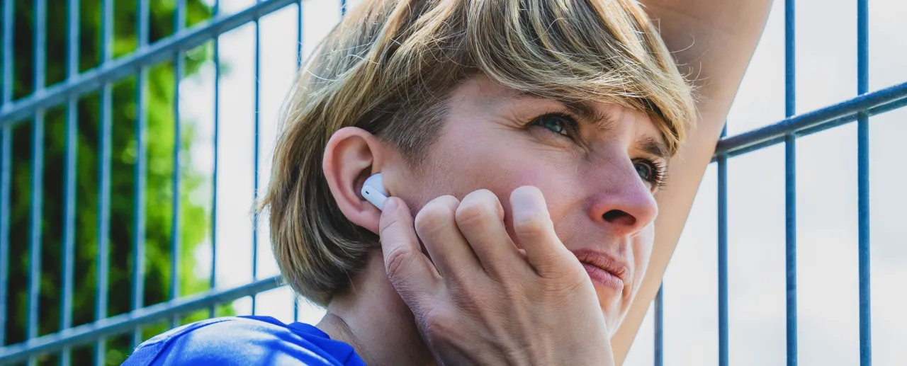 Kobieta z blond włosami wkłada białą słuchawkę do ucha, pokazując, jak sparować słuchawki.