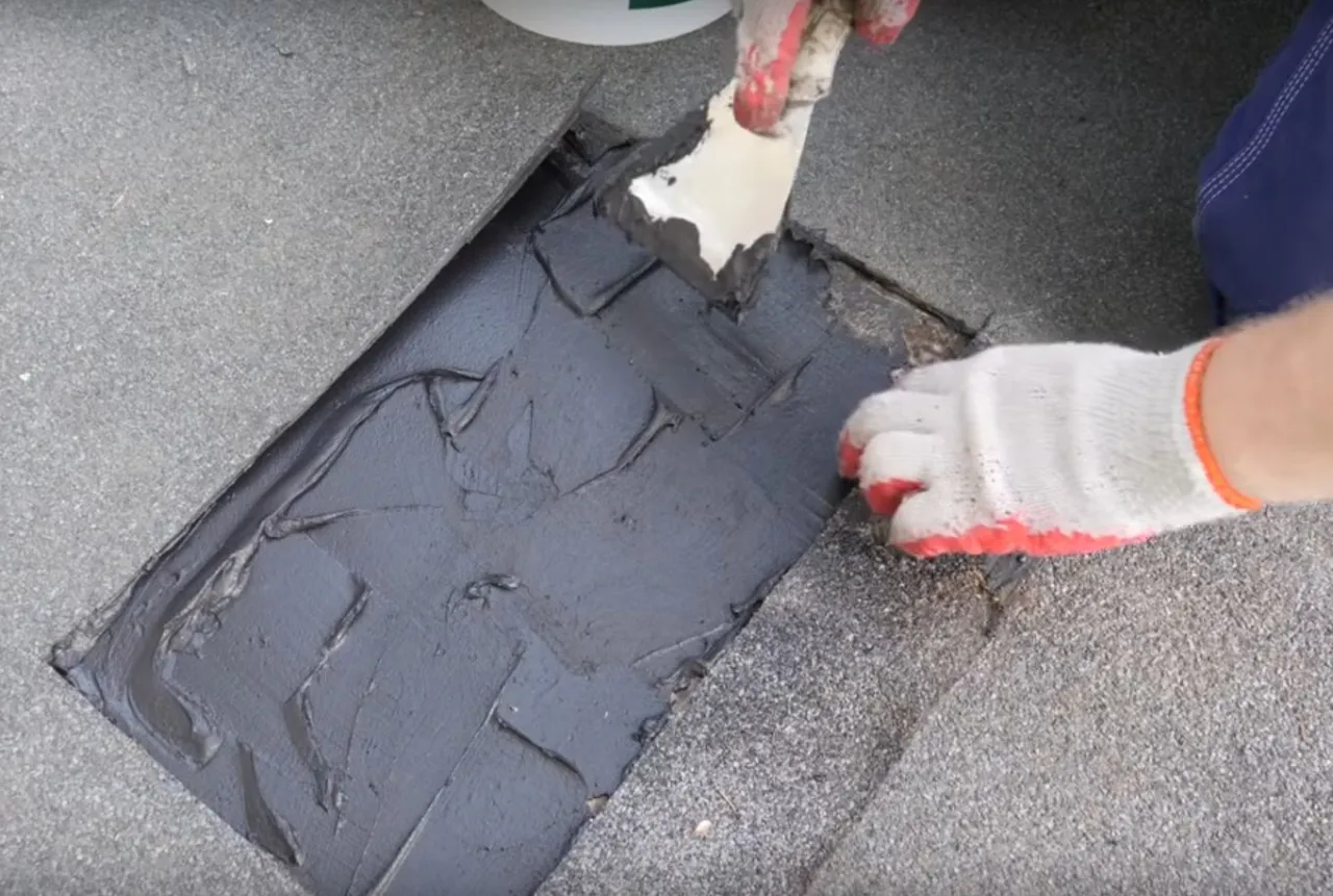 Naprawa dachu pokrytego papą: nakładanie masy uszczelniającej na uszkodzony fragment.