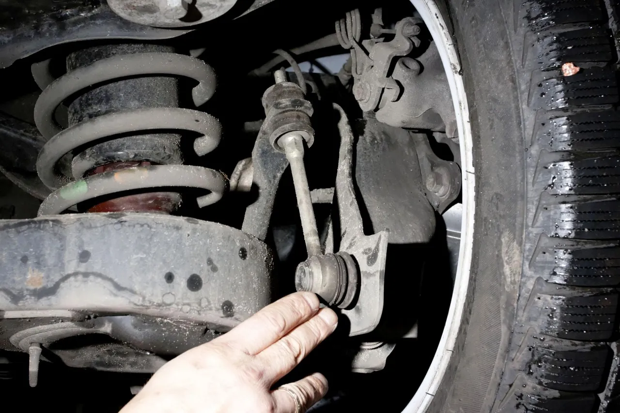 Dłoń wskazuje na łącznik stabilizatora, kt&oacute;ry odpowiada za stabilność pojazdu podczas pokonywania zakręt&oacute;w.