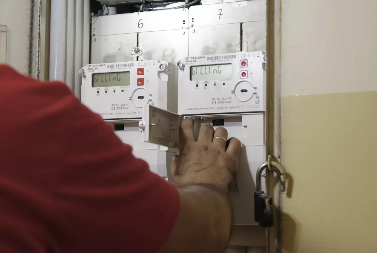 Ręka otwiera klapkę licznika prądu. Widać dwa liczniki z cyfrowymi wyświetlaczami.
