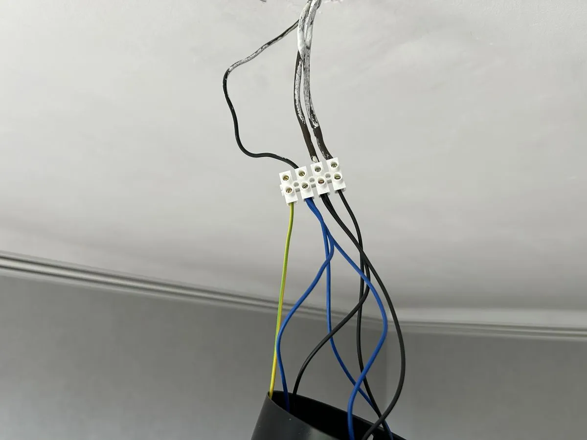 Podłączanie żyrandola: 3 kable z sufitu połączone w kostce. Widać przewody czarny, niebieski i żółto-zielony.