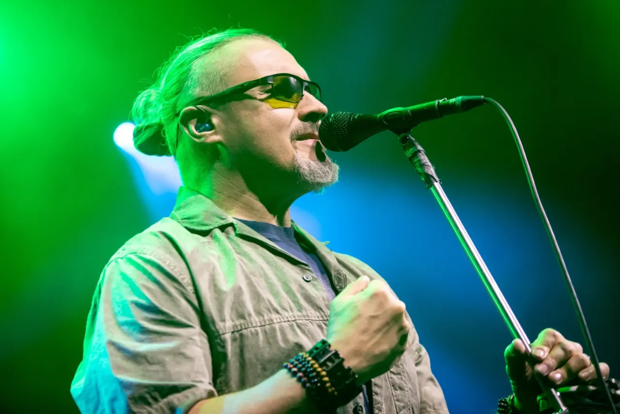 Artysta z charakterystycznym kucykiem i okularami śpiewa do mikrofonu. Czy to on śpiewa 