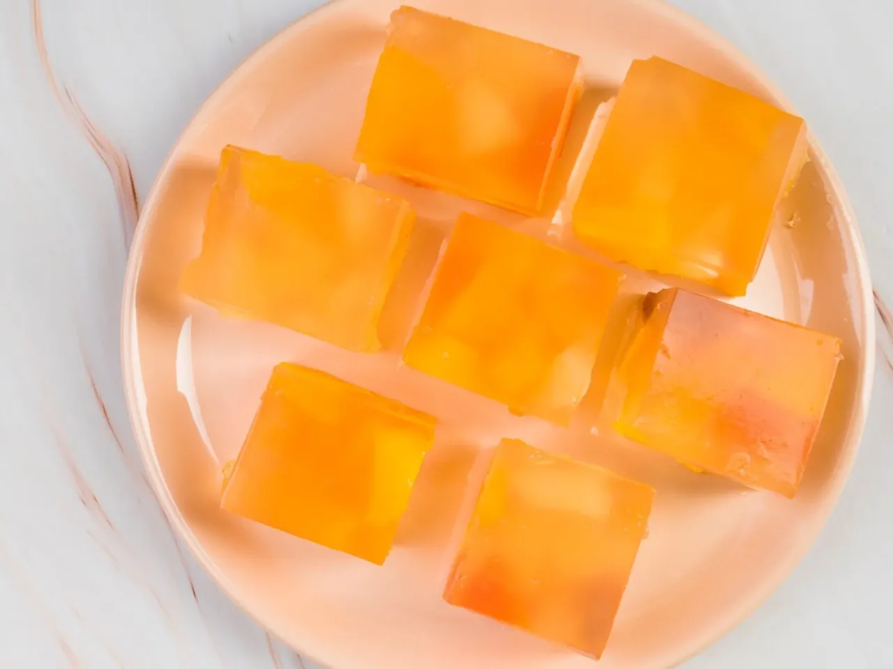 Pomarańczowe kostki galaretki z owocami na talerzu. Czy w galaretce jest kolagen?