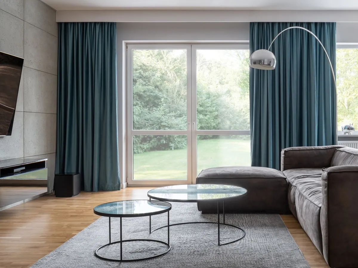 Nowoczesne zasłony w odcieniu głębokiego turkusu, zawieszone na ukrytych karniszach, podkreślają elegancję salonu. To pokazuje, jakie karnisze są modne.