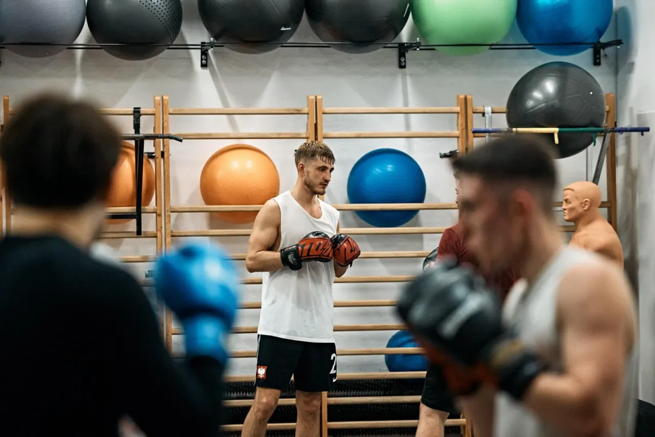 Trening boksu w Łodzi. Mężczyźni w rękawicach bokserskich, piłki gimnastyczne w tle. Idealne miejsce, gdzie trenować crossfit w Łodzi.