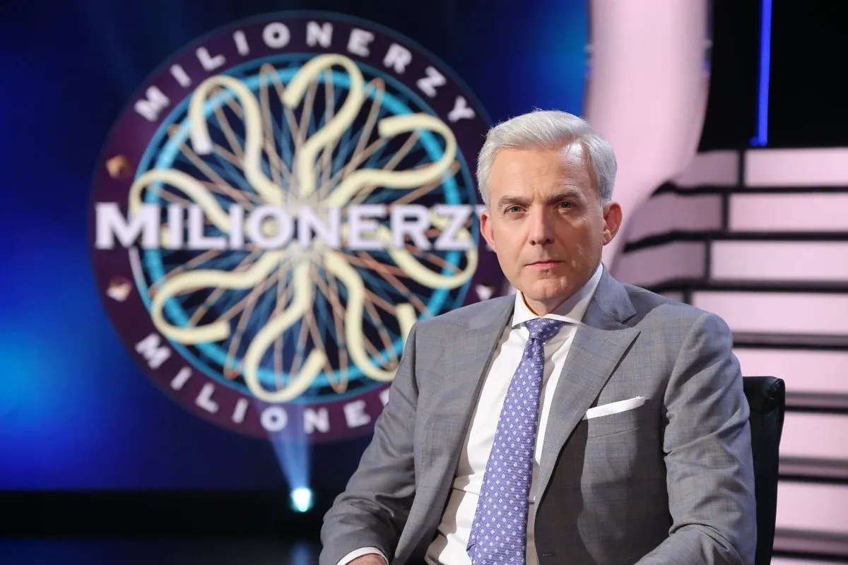 Prowadzący w garniturze siedzi przed kołem 