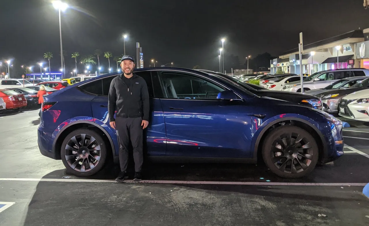 Mężczyzna stoi obok niebieskiej Tesli Y. Zastanawiasz się, ile waży Tesla Y?