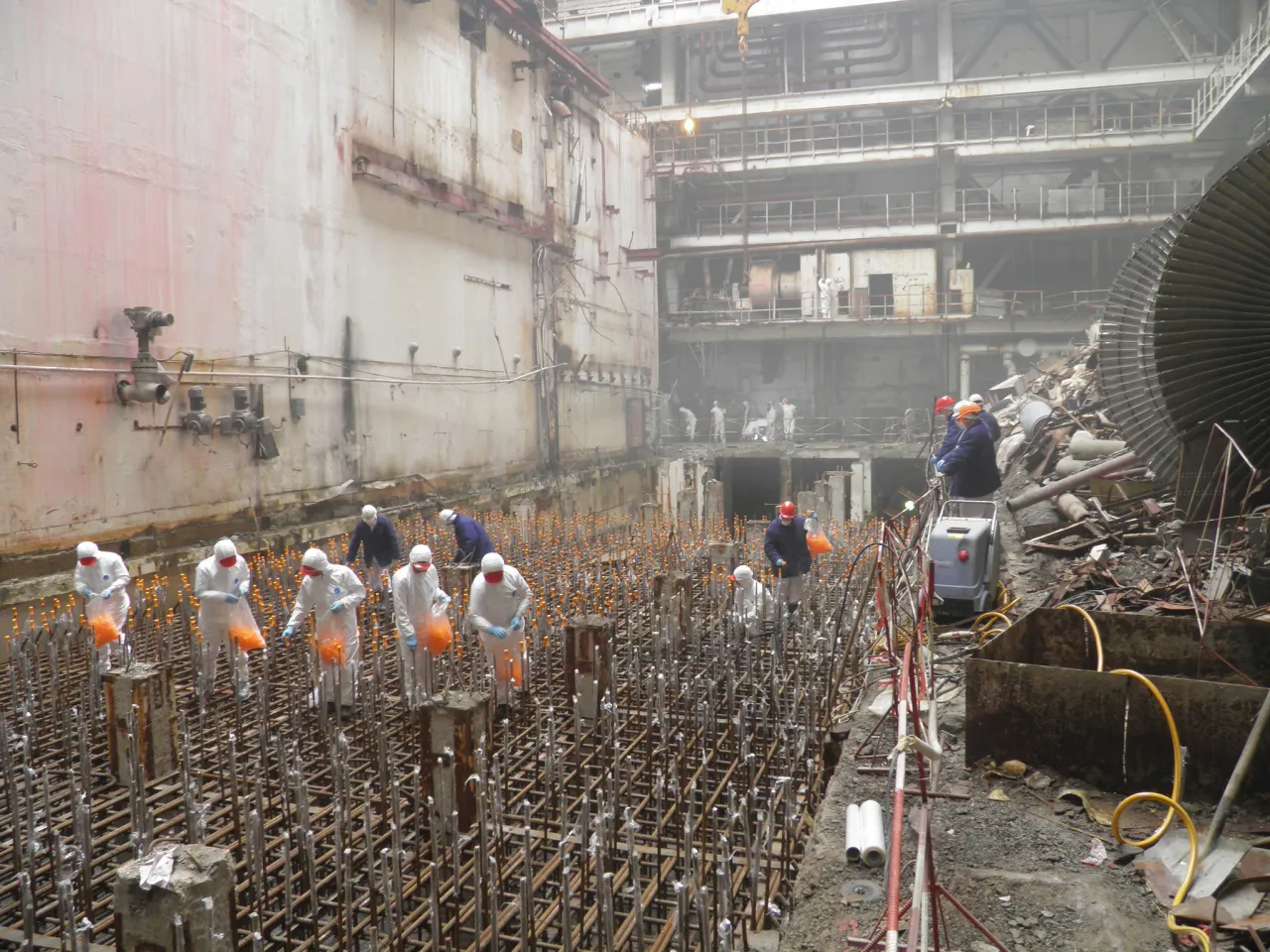 Pracownicy w kombinezonach ochronnych pracują przy zbrojeniu, zbliżając się do dnia, kiedy Czarnobyl będzie bezpieczny.