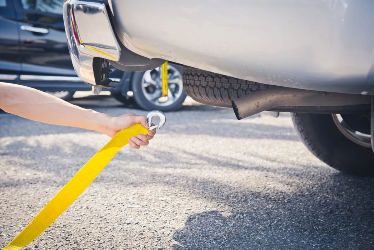 Ręka trzymająca ż&oacute;łtą linę do holowania, przygotowująca holowanie na autostradzie.
